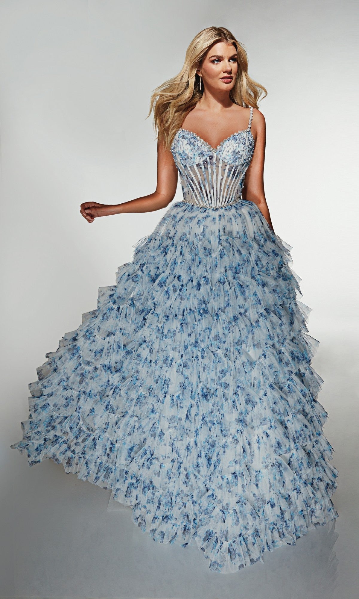 A woman wears the Alyce 62182 Long Prom Dress, a blue and white tiered floral ball gown with a sheer corset bodice and thin straps, standing against a plain background.